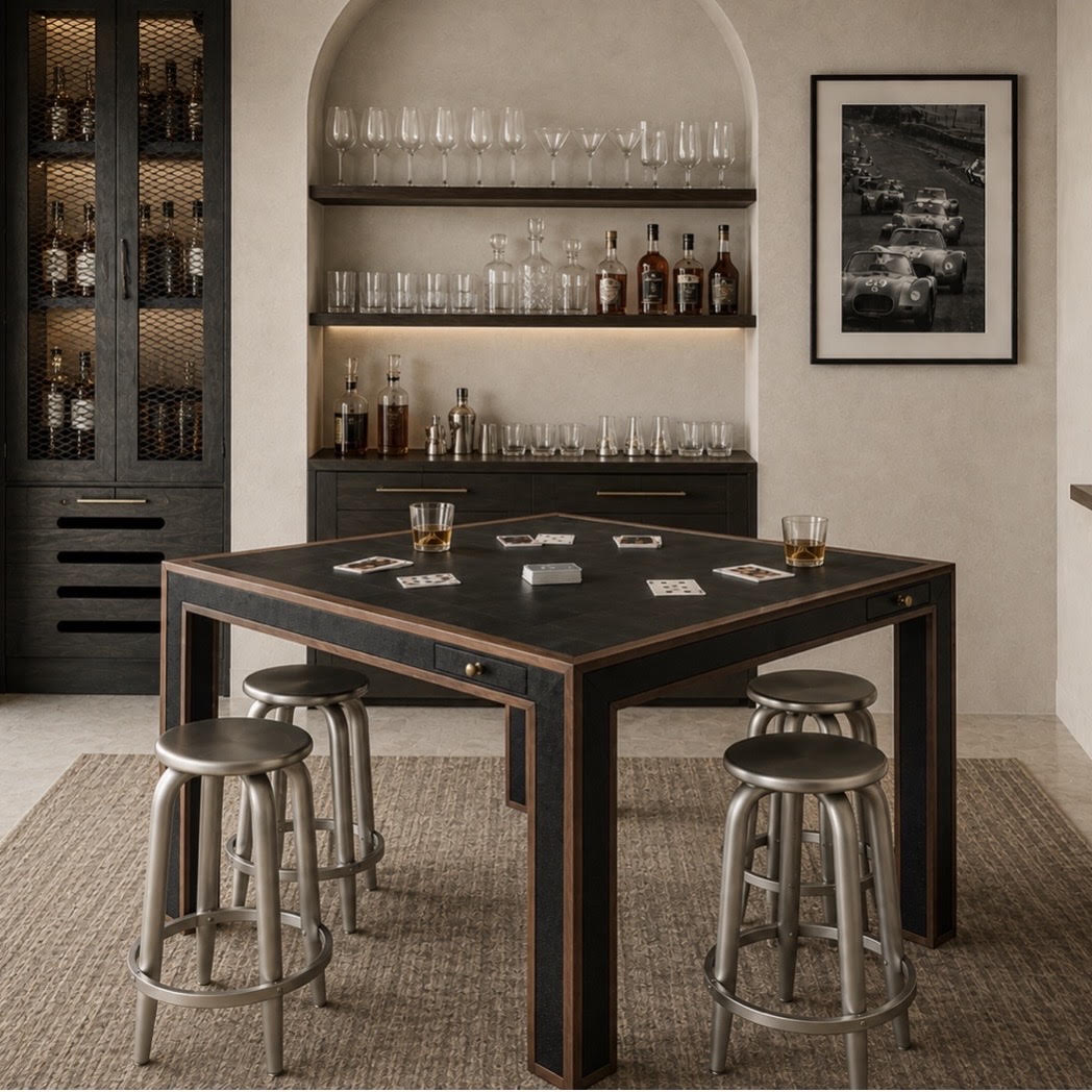 A dark wood and black bar table with six round silver metal bar stools, styled in a modern home bar setting with wine glasses, bottles, and glasses on the table.