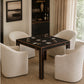 A dark wood square gaming table surrounded by four cream upholstered armchairs in a styled interior room with a window, curtains, and built-in shelving.