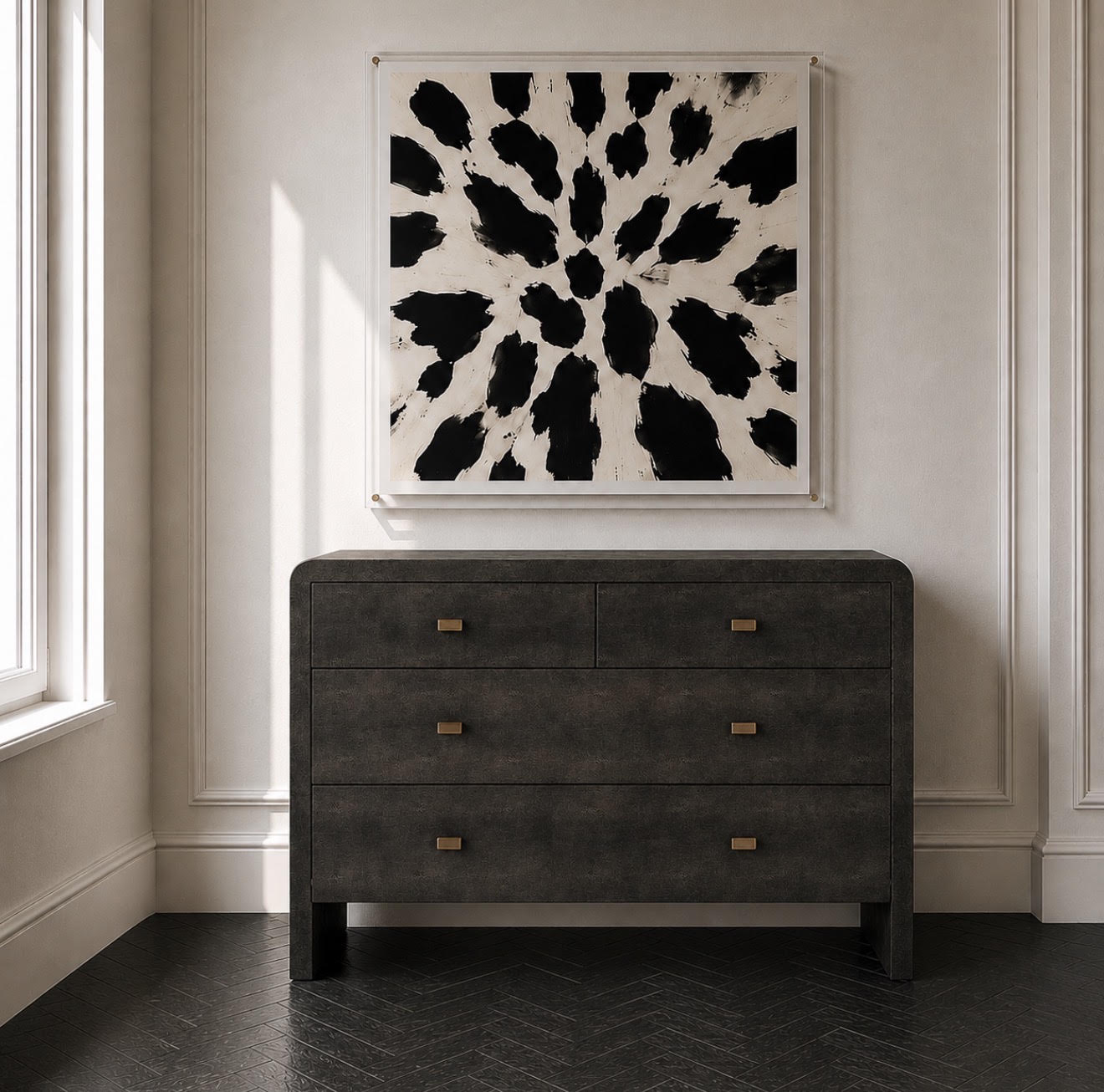 A dark charcoal gray wooden dresser with brass handles, positioned against a white paneled wall below a black and white abstract canvas print.