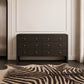 A dark charcoal gray dresser with six drawers and small brass handles, styled in a modern room with a zebra-print rug and a cream wall.