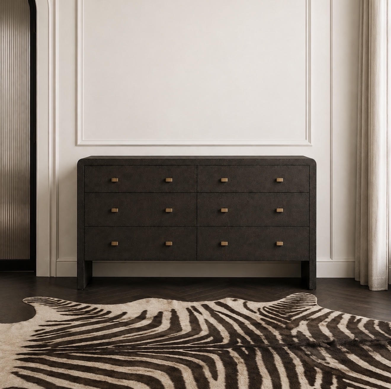 A dark charcoal gray dresser with six drawers and small brass handles, styled in a modern room with a zebra-print rug and a cream wall.