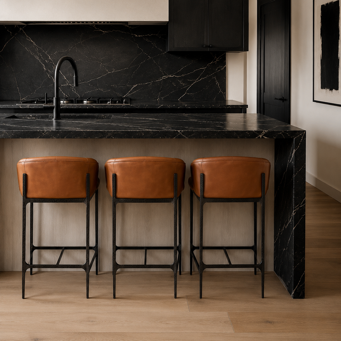A modern kitchen island with a black marble countertop and backsplash, paired with three brown leather bar stools with black metal frames. The room features light wood flooring and neutral beige walls.