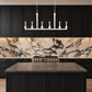 A modern kitchen scene with black cabinets, a white marble backsplash, a dark stone countertop island, and a white multi-light pendant chandelier hanging above the island.