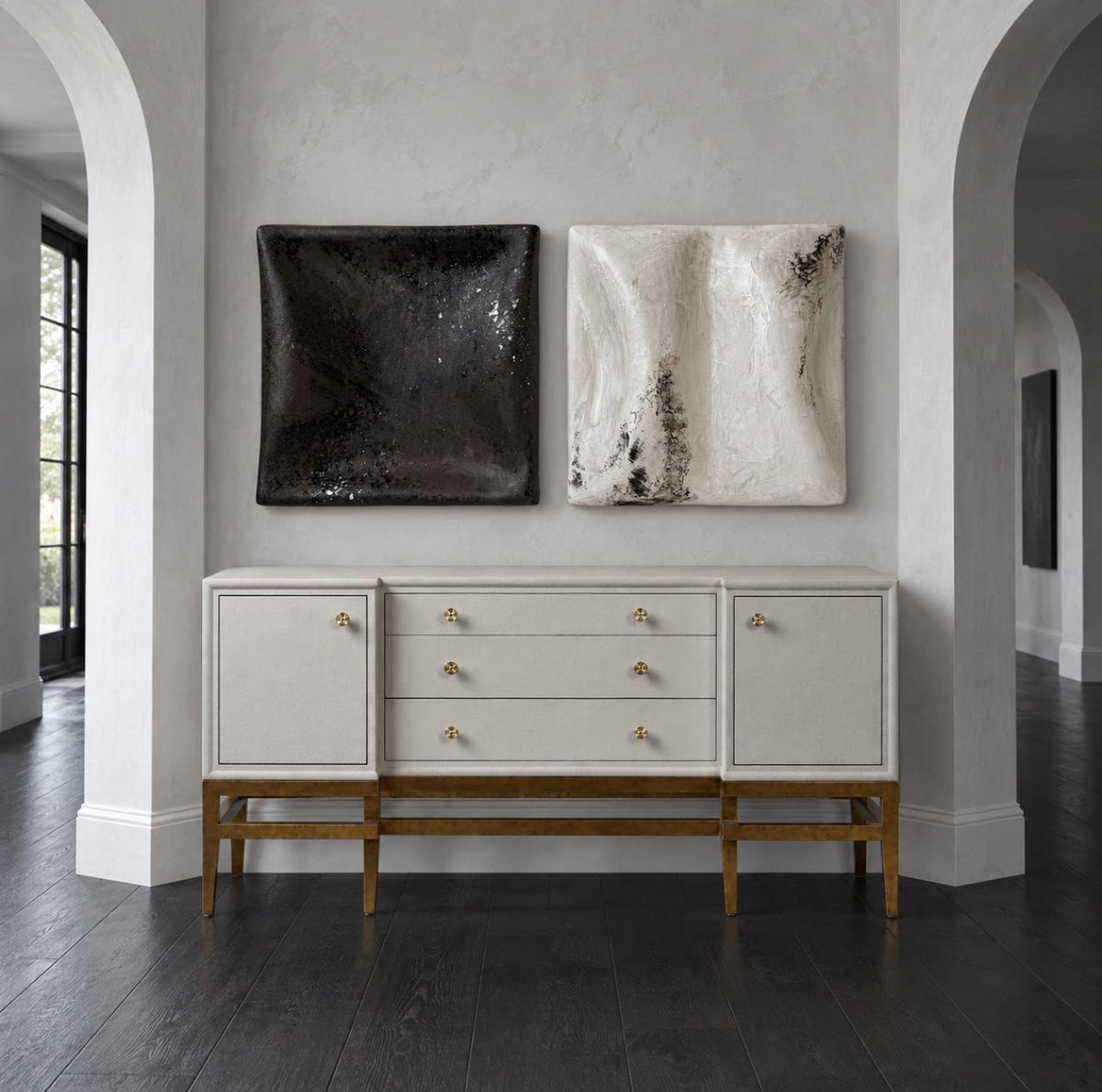 A mid-century modern sideboard console with a warm off-white painted finish and a natural wood base, styled in a minimalist interior with two abstract wall art pieces above it.