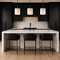A modern kitchen island with a white marble-look countertop and matching backsplash, surrounded by three black leather bar stools with black metal frames. The background features black cabinetry, a black range hood, and three black pendant lights hanging above.