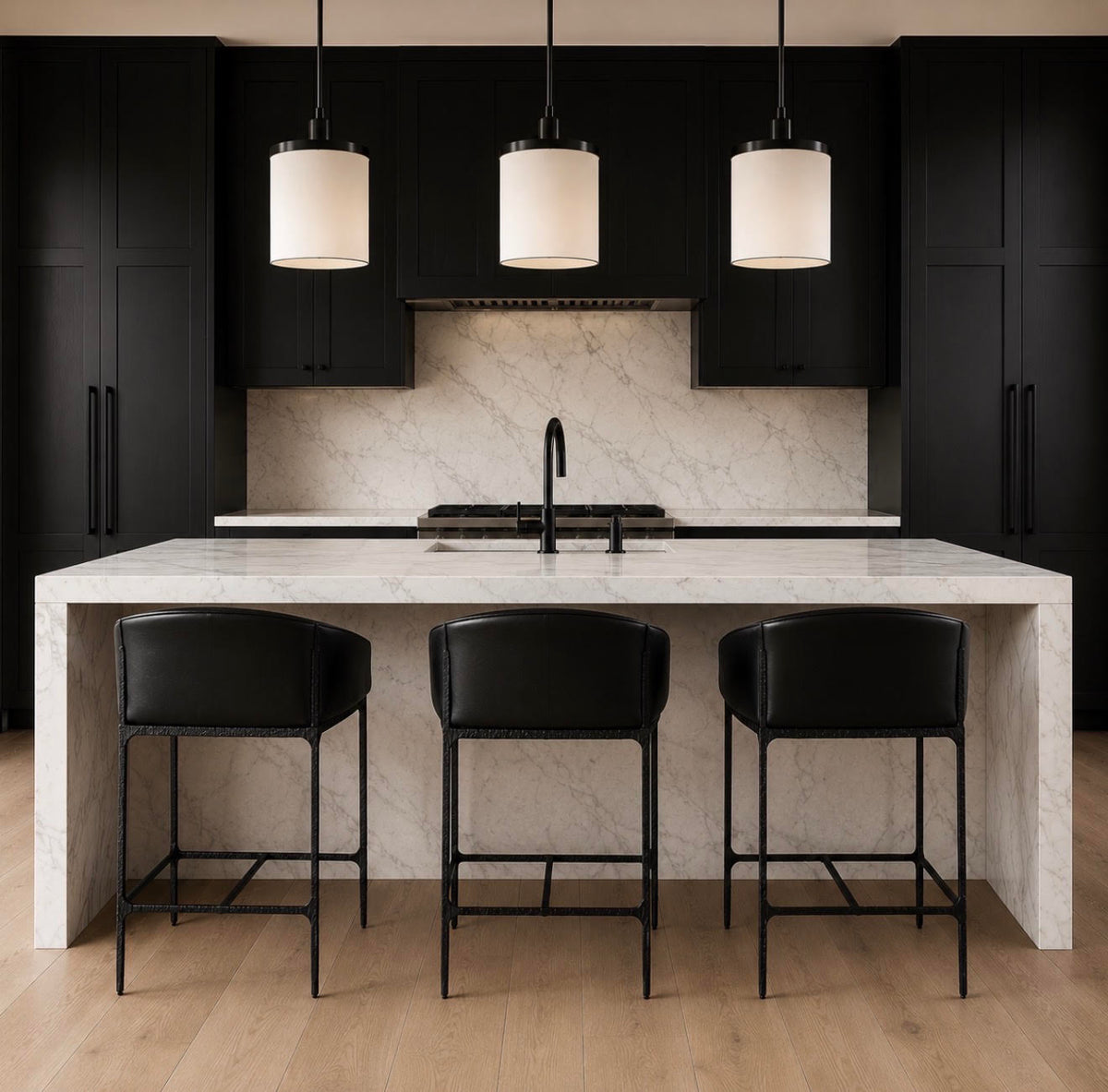 A modern kitchen island with a white marble-look countertop and matching backsplash, surrounded by three black leather bar stools with black metal frames. The background features black cabinetry, a black range hood, and three black pendant lights hanging above.