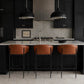 A modern kitchen island with a gray stone countertop, black cabinetry, two black pendant lights, and three brown leather bar stools with black metal frames.