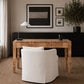 A rustic wooden writing desk with a white upholstered chair in a styled home office setting, featuring a black sideboard, framed wall art, and a table lamp.