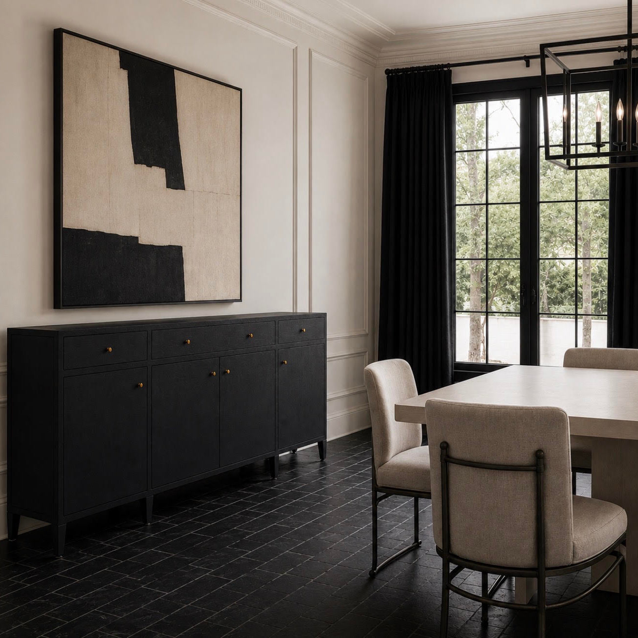 A modern dining room corner featuring a dark charcoal sideboard cabinet with brass knobs, a large abstract black and beige wall art piece, black-framed windows with dark curtains, and upholstered dining chairs.