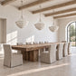 A rustic dining room scene featuring a long wooden dining table surrounded by upholstered chairs, with three woven pendant lights hanging from exposed wooden ceiling beams.