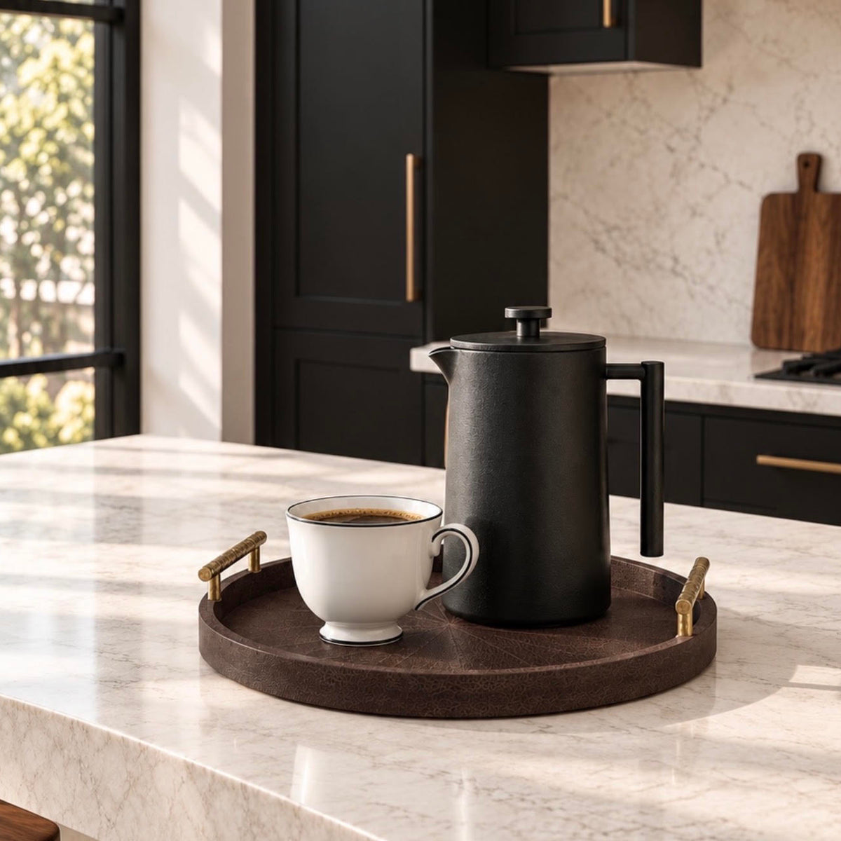 A round dark brown wooden serving tray with gold-toned handles, holding a black coffee maker and a white ceramic cup on a white marble kitchen counter.