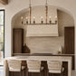A rustic wood candelabra-style pendant light with six lit candle sleeves hangs above a kitchen island in a warm, modern kitchen with stone walls and dark wood cabinetry.