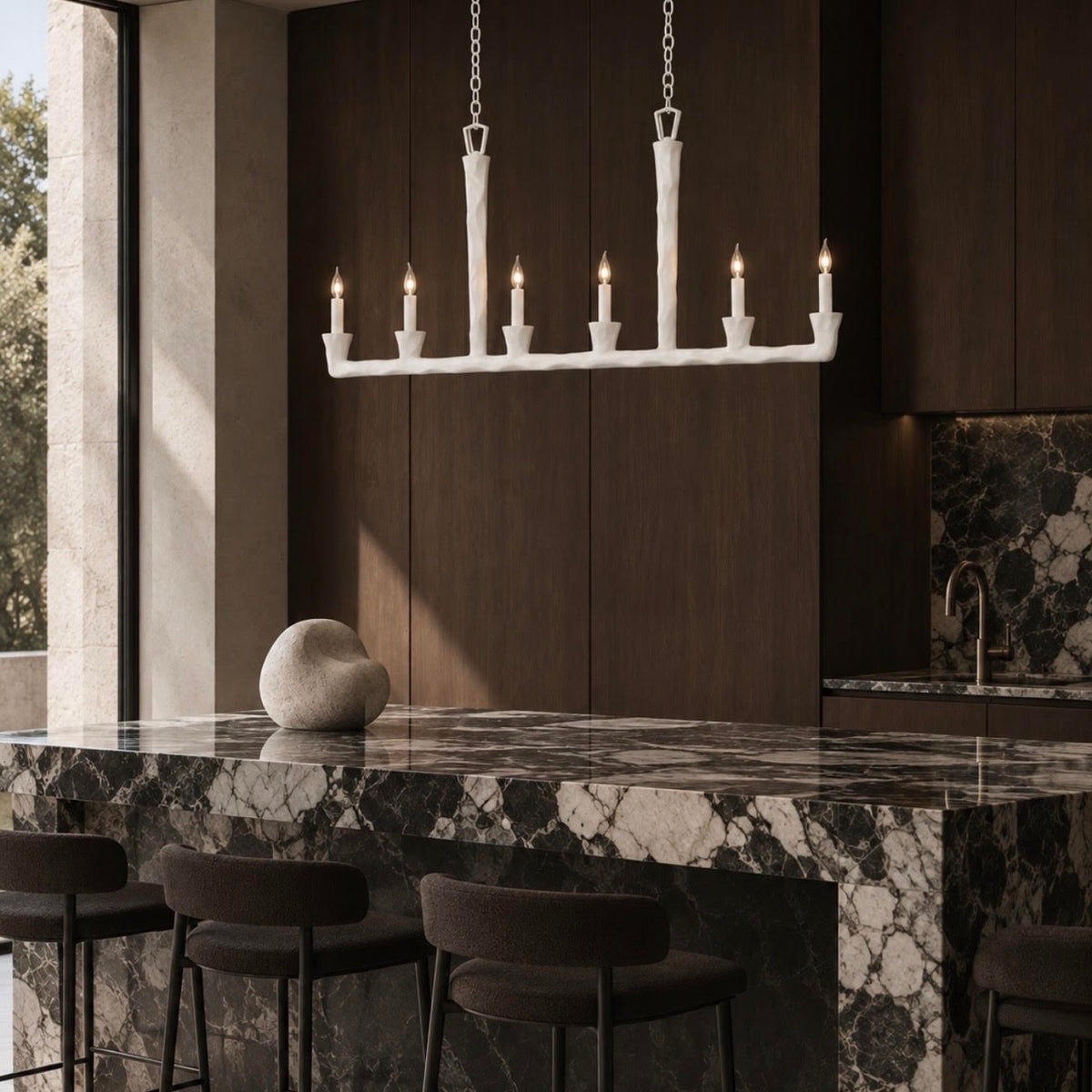 A white candelabra-style pendant chandelier with six candle-shaped bulbs hangs over a dark marble kitchen island in a modern kitchen setting with dark wood cabinetry and bar stools.