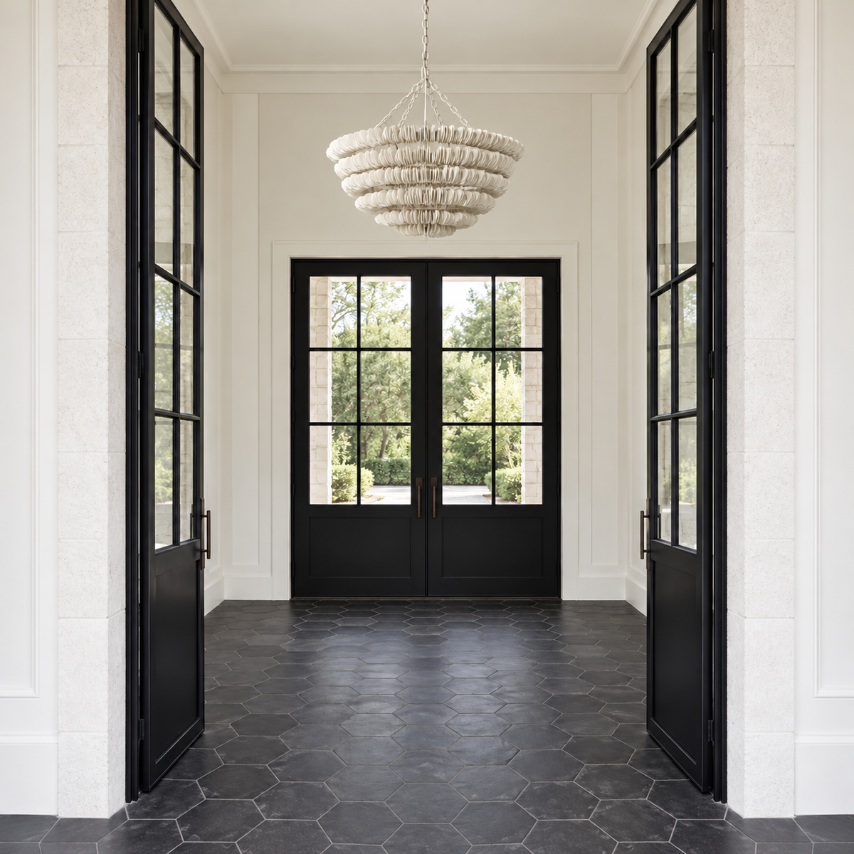 A modern entryway with black-framed glass doors, black hexagonal tile flooring, textured white walls, and a tiered white woven chandelier hanging in the center.