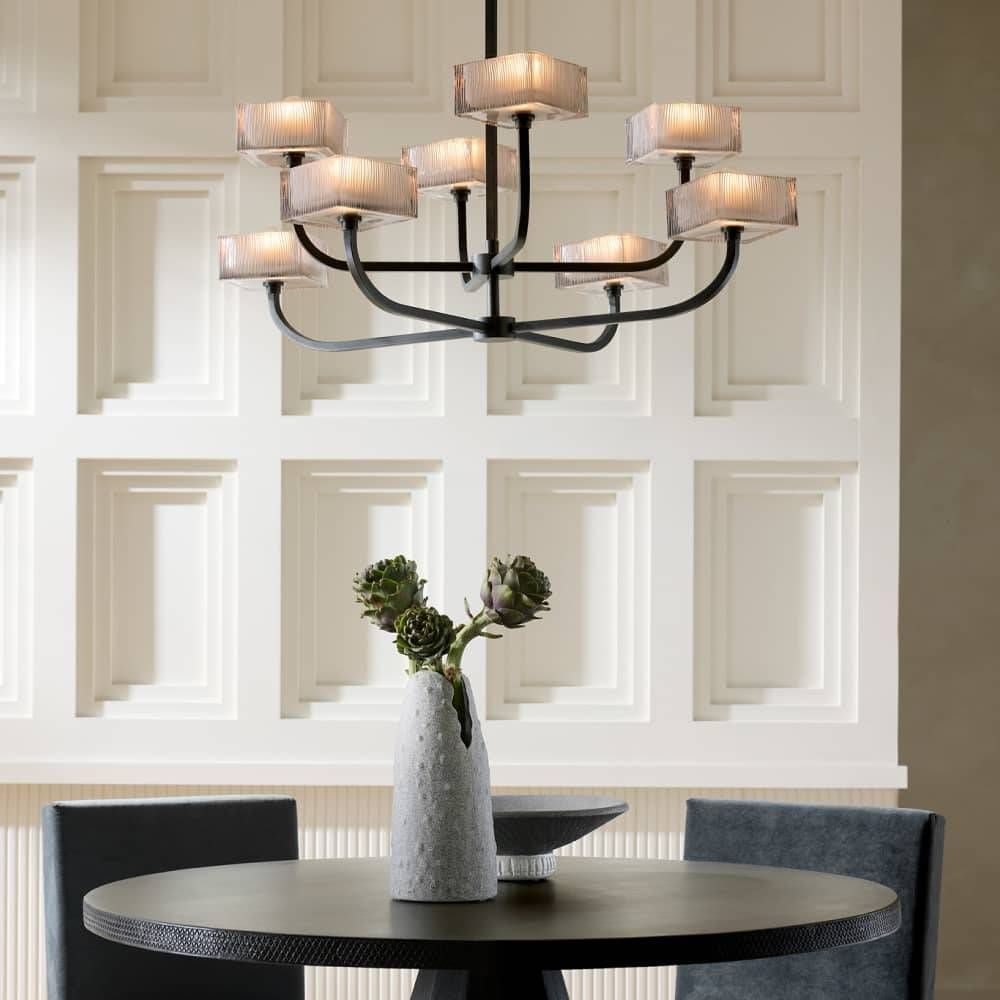 Chandelier hanging above a dining table with a vase of flowers in a room with decorative wall paneling.