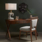 Wooden desk with chair, lamp, and decorative items against a dark wall.
