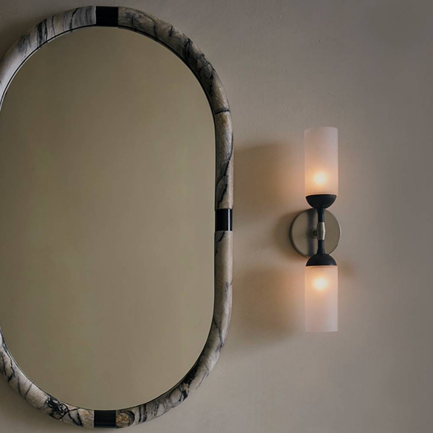 Round mirror with decorative frame on a wall next to a sconce.