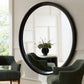 Large round mirror with black frame in a room with chairs and a table.