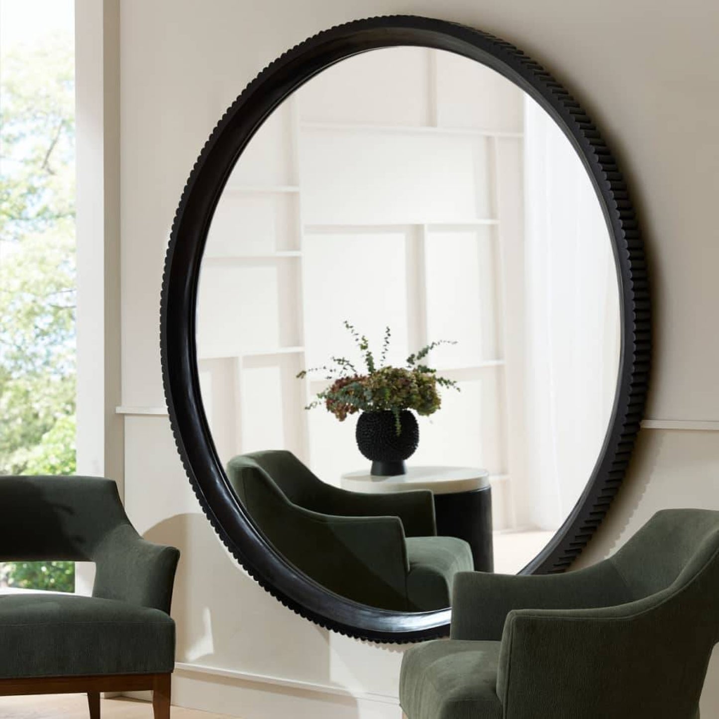Large round mirror with black frame in a room with chairs and a table.