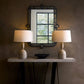 Two table lamps on a stand with a decorative mirror above them against a textured wall.