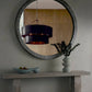 Round mirror with decorative frame on a wall above a console table with a vase and bowl.