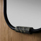 Close-up of a mirror with a decorative black frame and metallic accent on a wooden surface.
