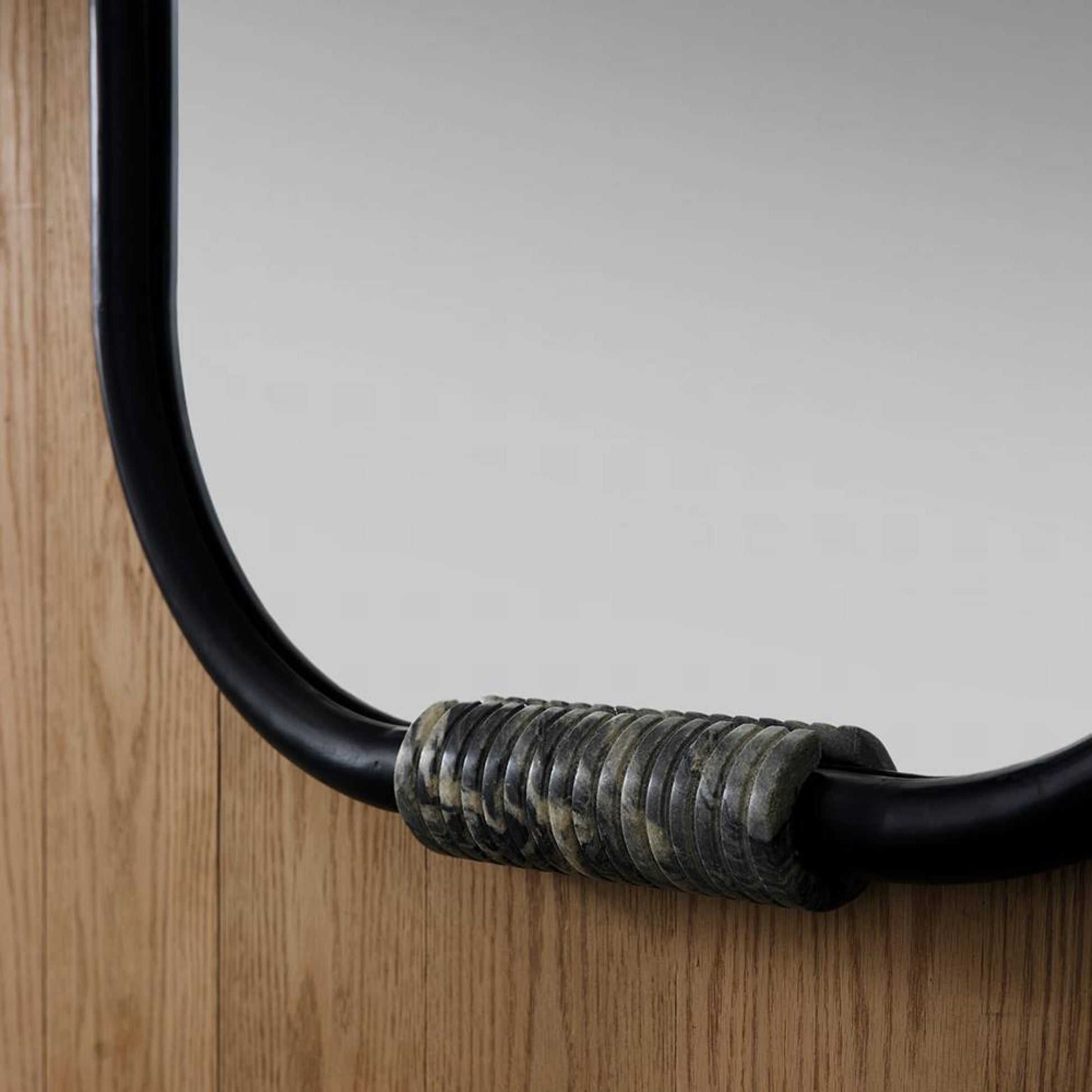 Close-up of a mirror with a decorative black frame and metallic accent on a wooden surface.
