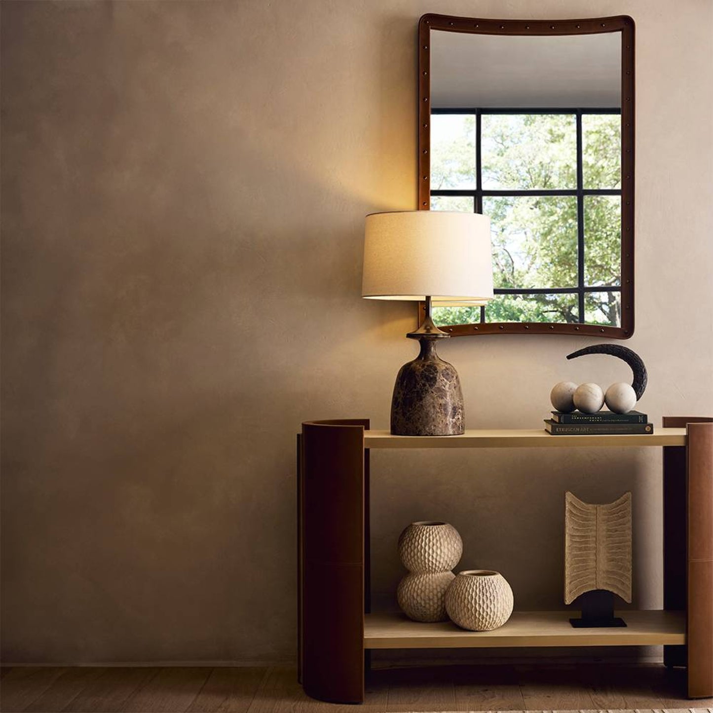 Decorative console table with lamp, mirror, and sculptures against a beige wall.