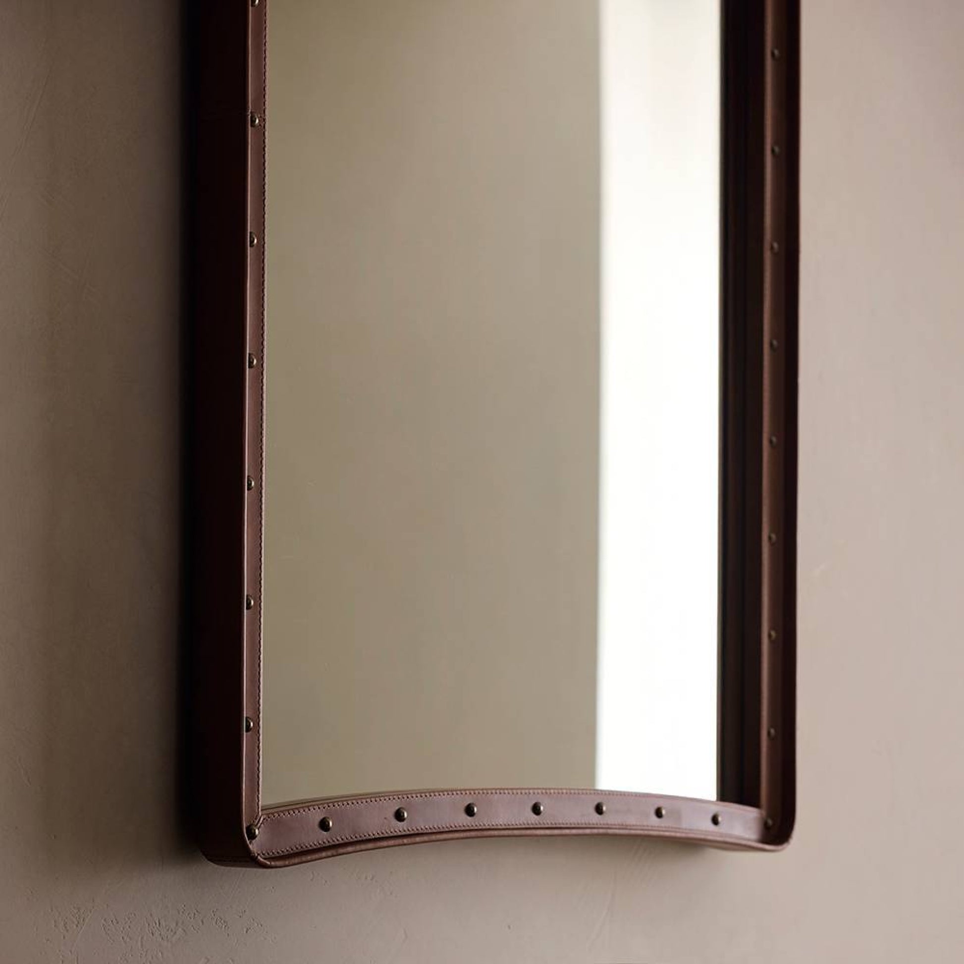 Rectangular mirror with a brown leather frame on a beige wall.