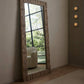 Large decorative mirror with geometric frame in a room with a white armchair and greenery outside.