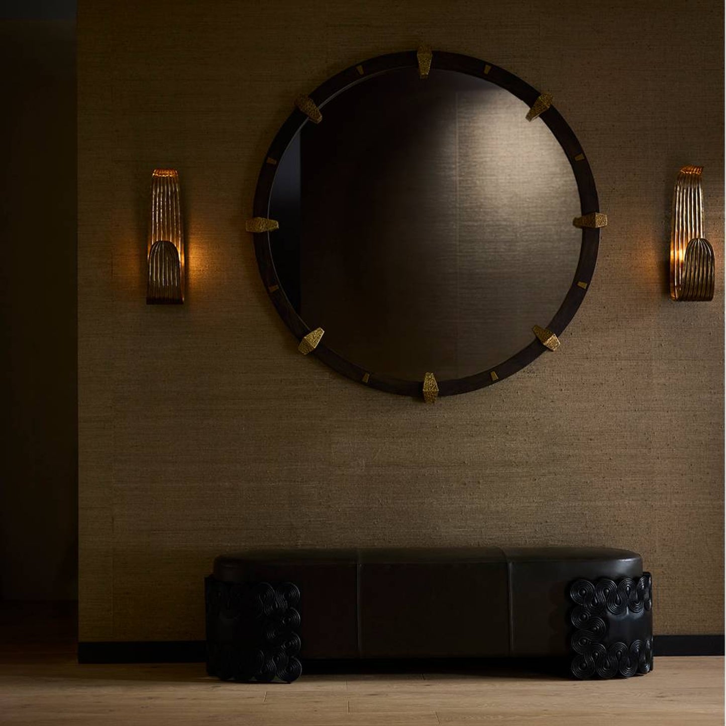 Round mirror with decorative frame on a textured wall with wall sconces.