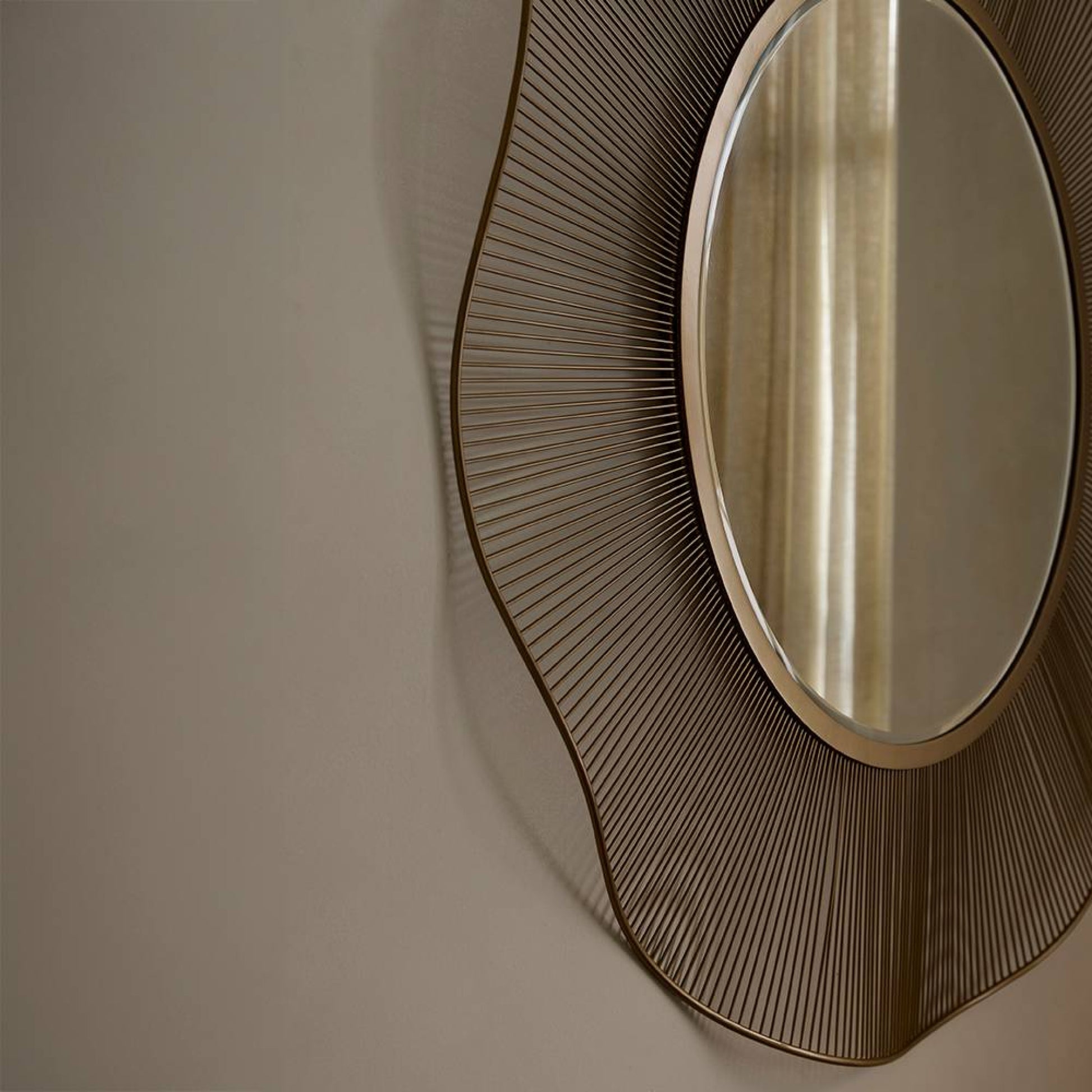 Decorative wall mirror with a brown, sunburst design on a beige wall.