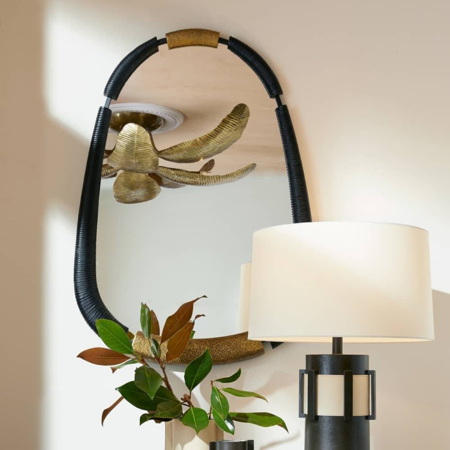 Decorative wall mirror with black frame and gold accents, next to a lamp with white shade and black base.
