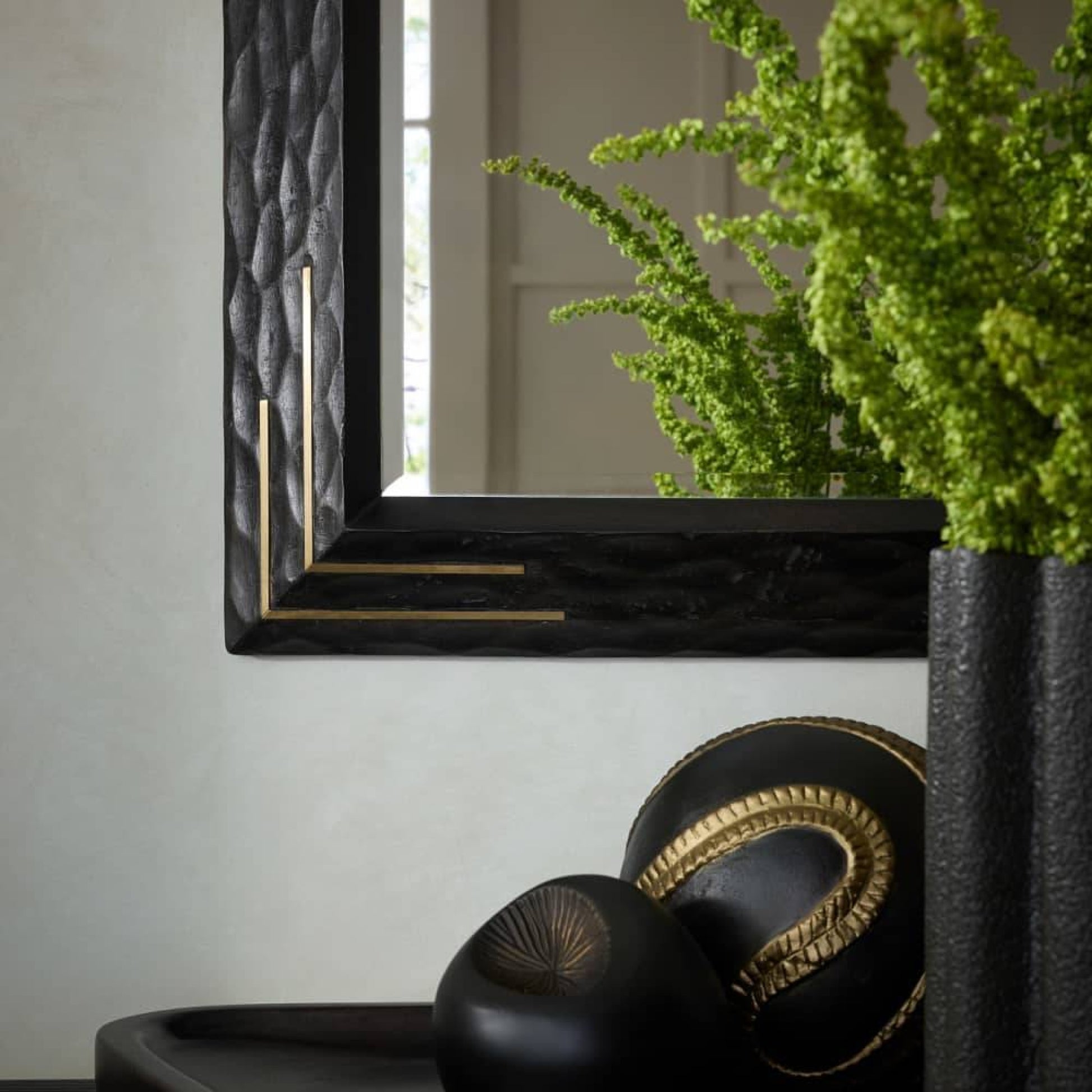 Decorative black and gold mirror with a plant on a gray wall