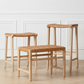 Four wooden stools with woven seats against a white paneled wall.