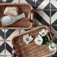 Wicker trays with flowers and a bottle on a black and white tiled floor
