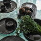 Black ceramic dishes on a textured green surface with greenery.