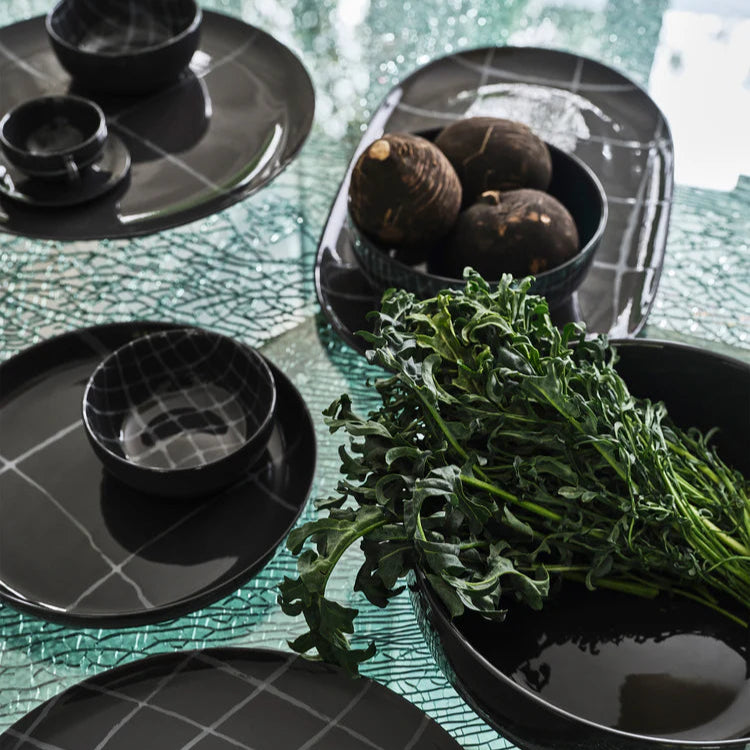 Black ceramic dishes on a textured green surface with greenery.
