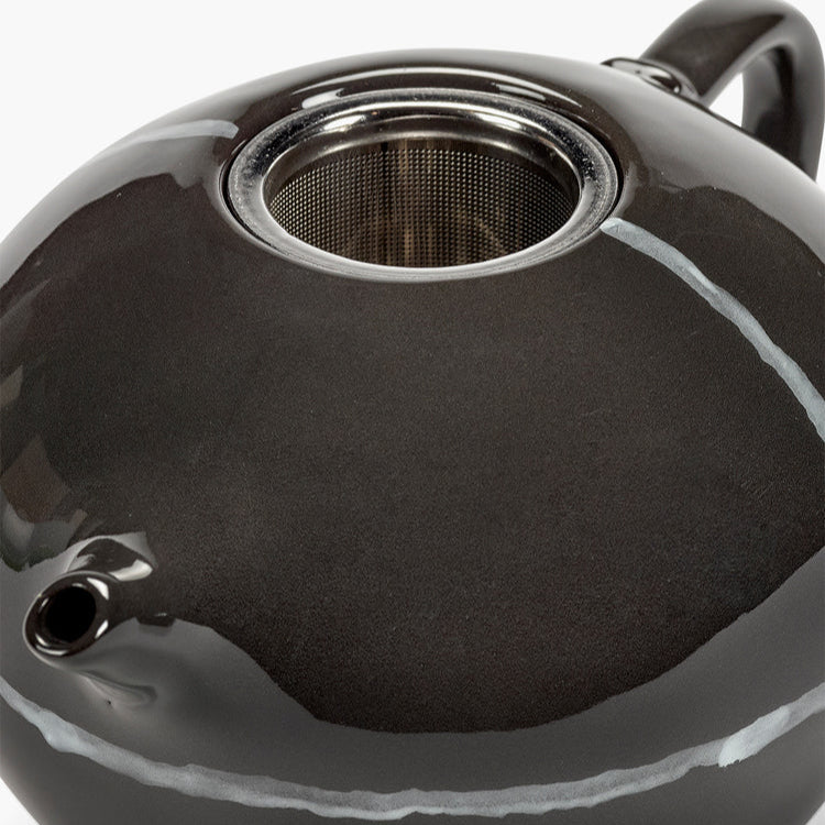 Close-up of a black ceramic teapot with metal mesh lid on a white background